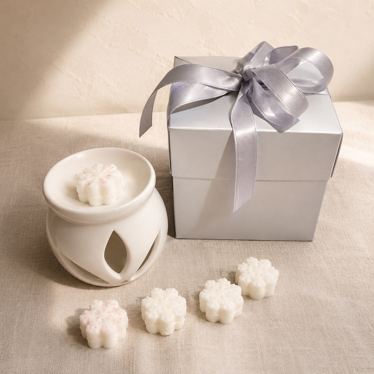 Silver gift box with a satin bow, a white ceramic burner and snowflake shaped wax melts