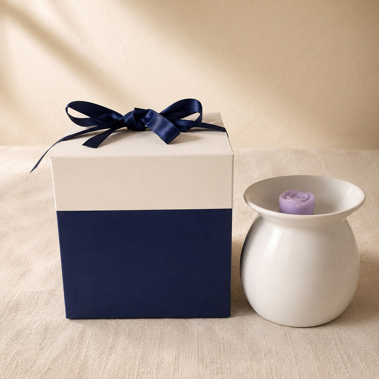 Navy and cream gift box with a navy ribbon bow beside a white ceramic wax burner