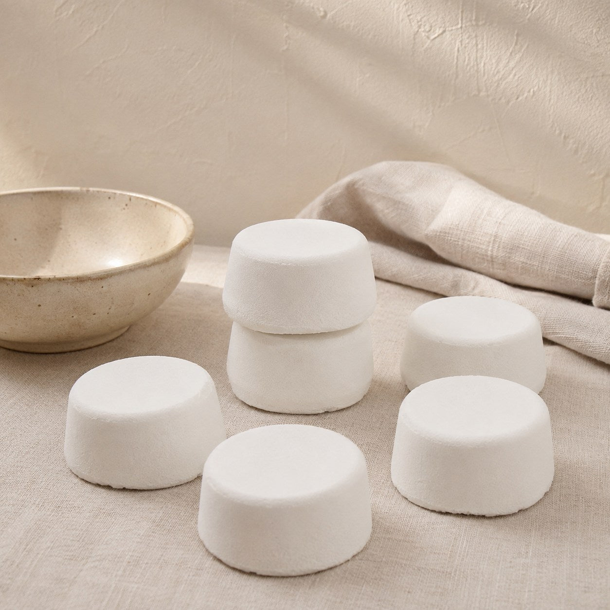 Six round white scented mop fizzer tablets on pale linen