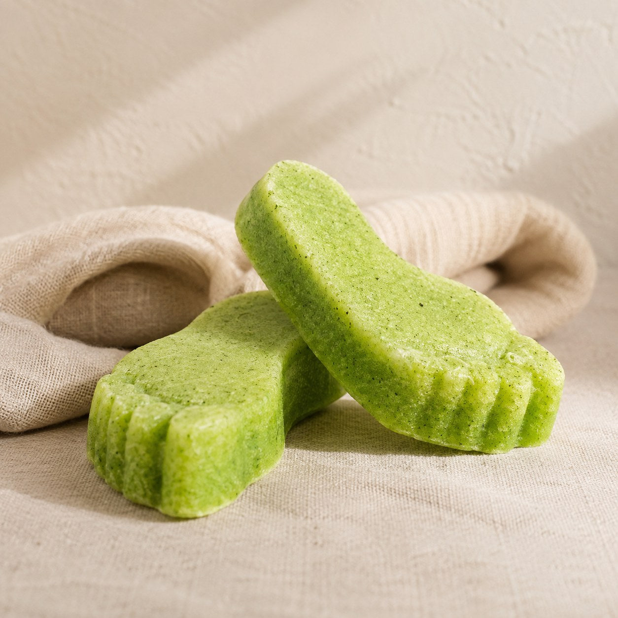 Green foot shaped pumice exfoliating soap bars on pale linen