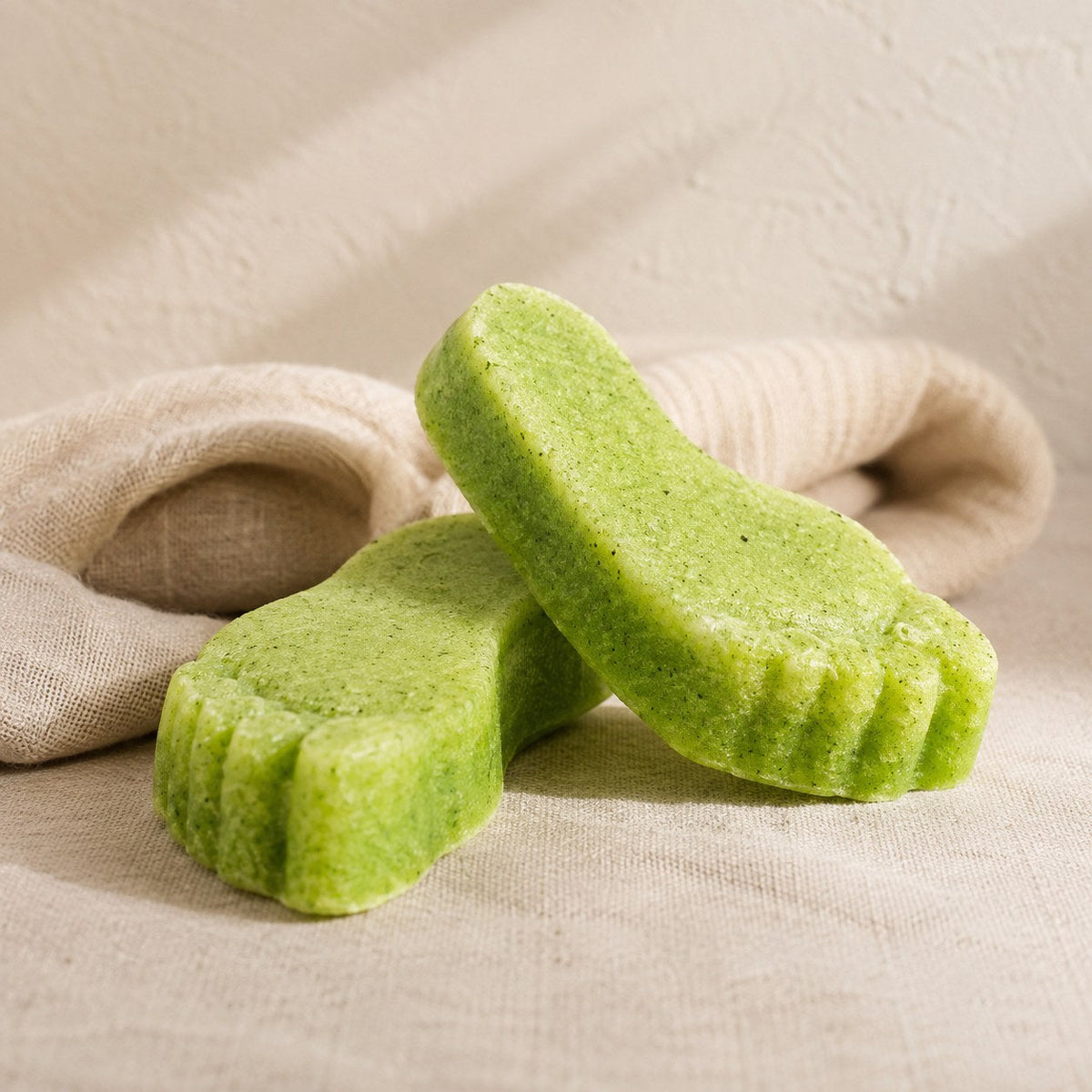 Green foot shaped pumice exfoliating soap bars on pale linen